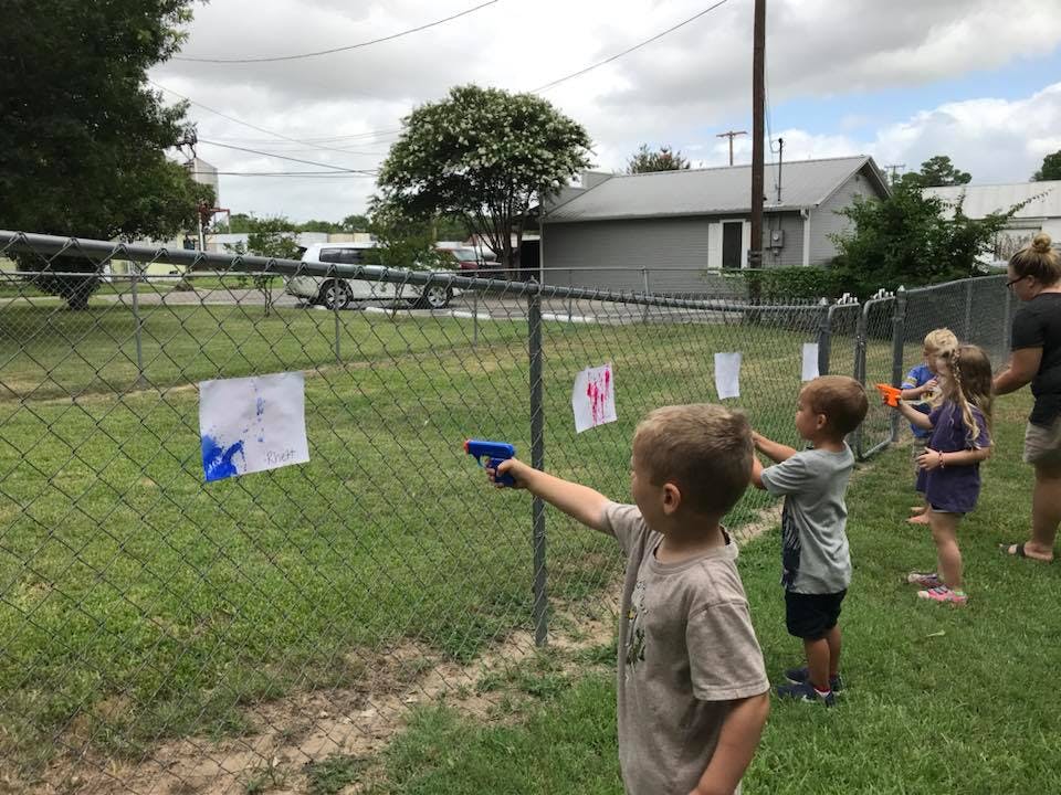 Children playing with water guns at targets on a fence