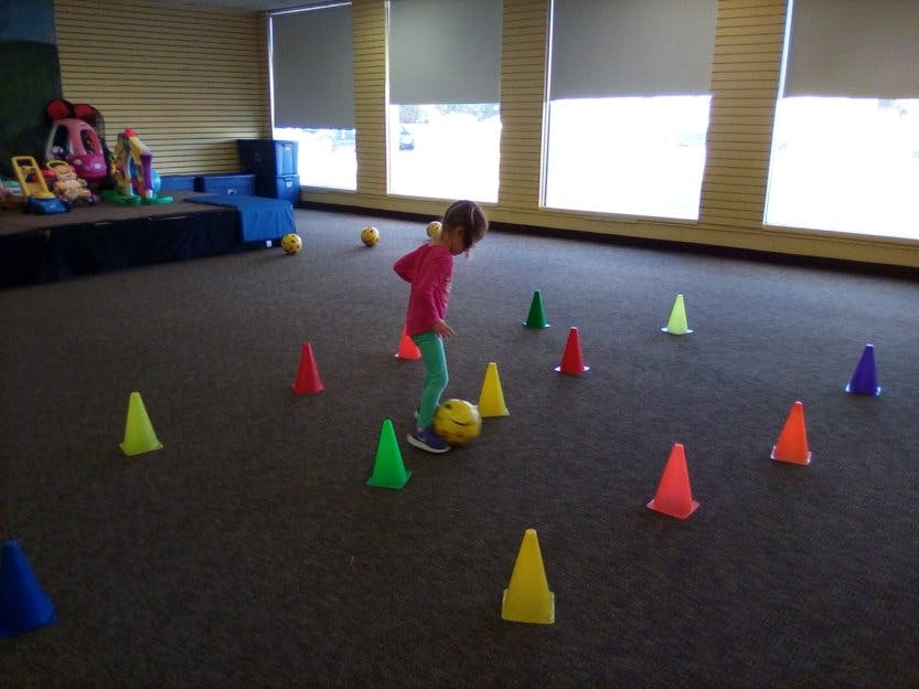Child playing with a yellow ball and colorful cones indoors