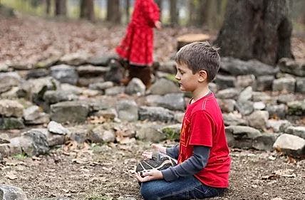 Child sitting on ground holding a rock, another child in background