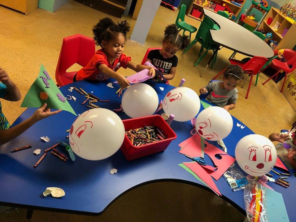 Children decorating balloons at a table in a classroom
