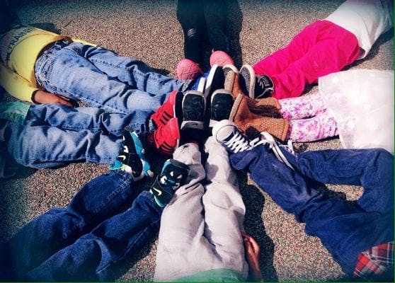 Children lying on the ground in a circle with their feet together