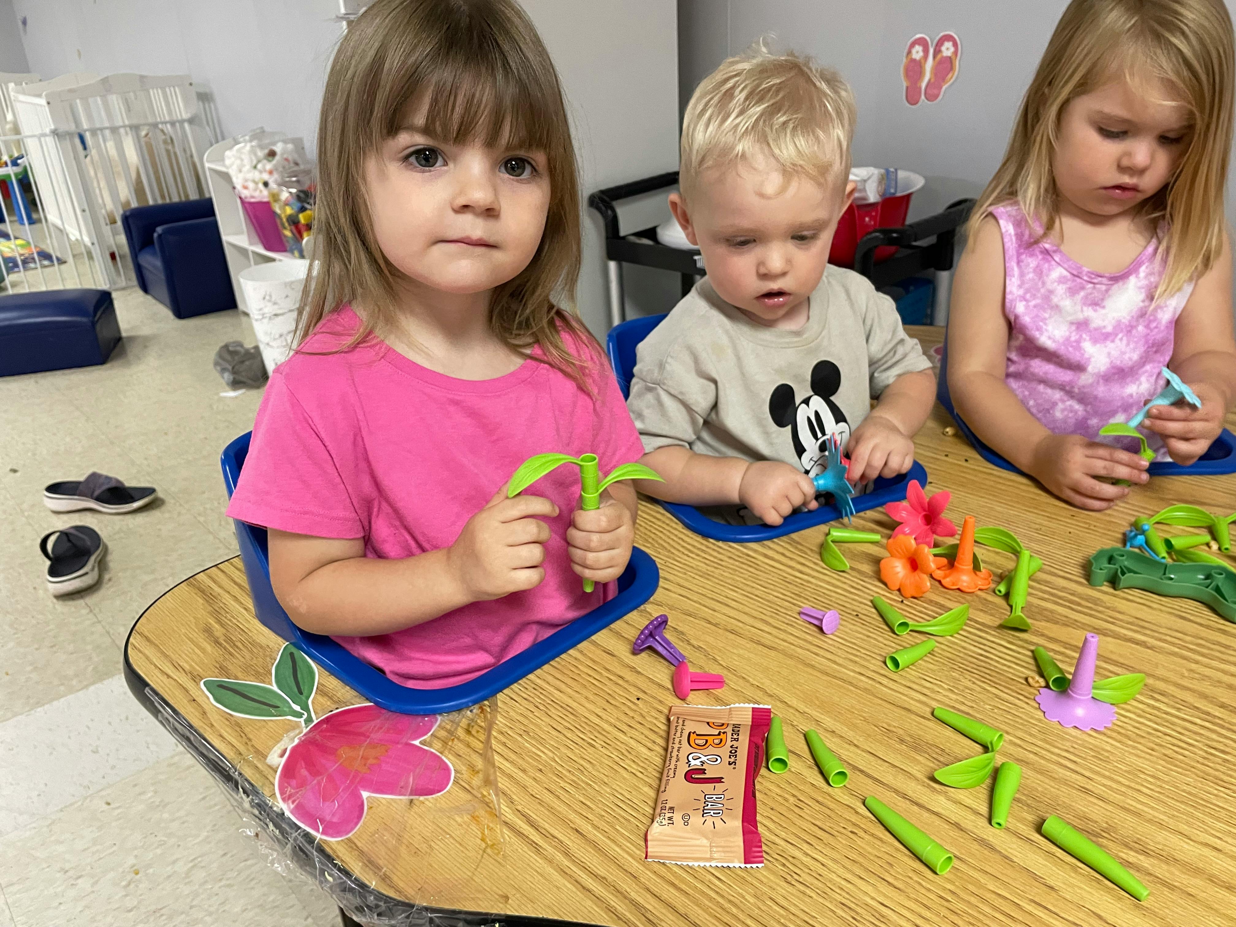 Three children playing with toy plants at a table