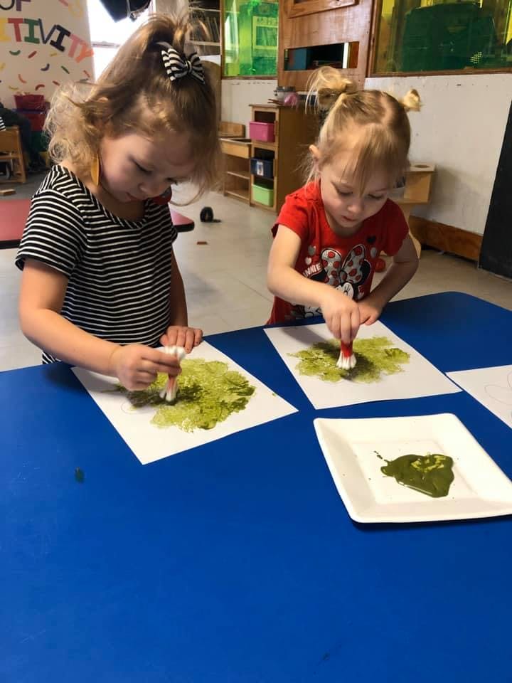 Two children painting with green paint on paper