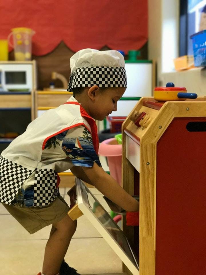 Child in chef's hat and apron opening a toy oven