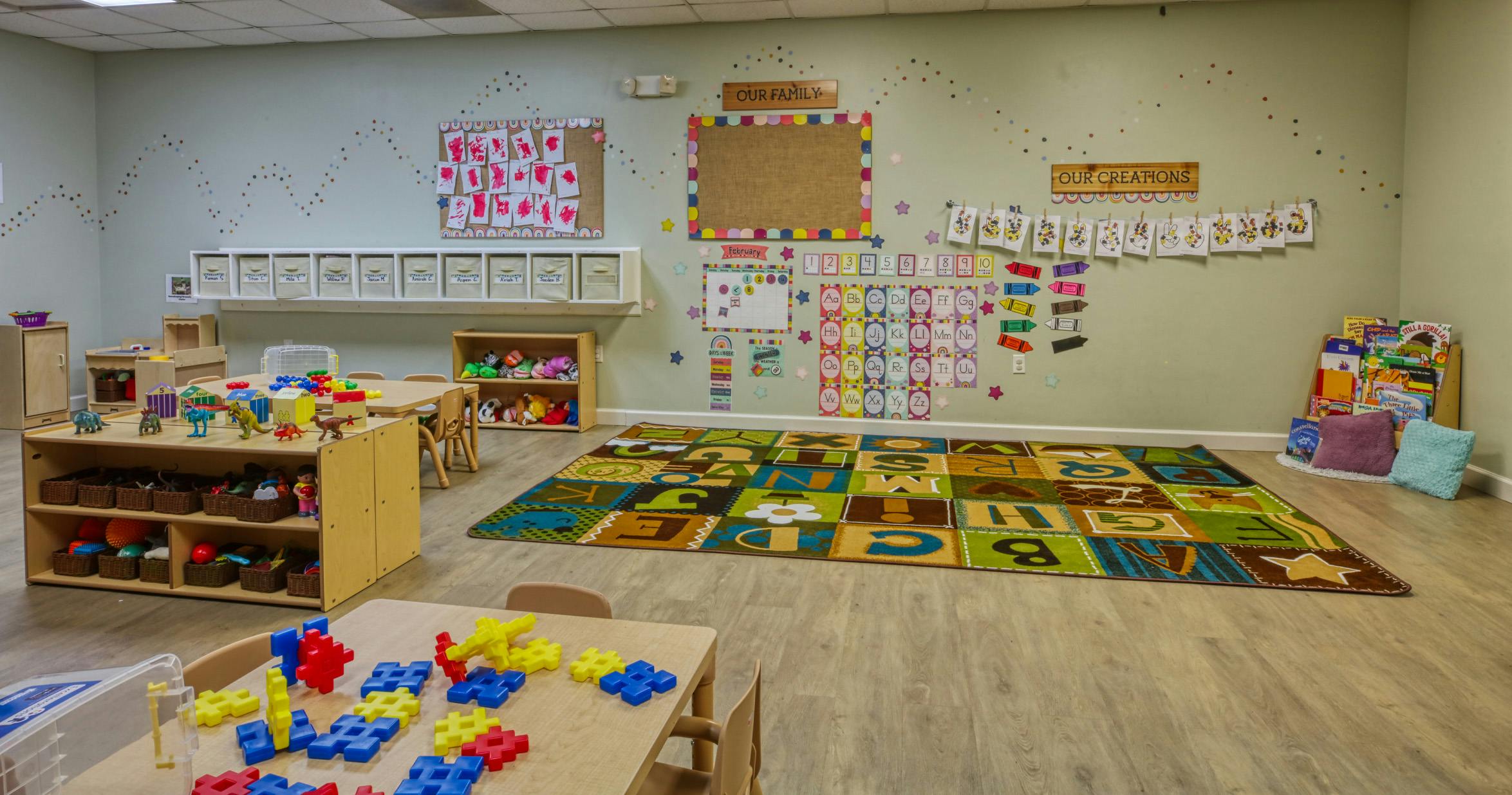 Children's classroom with alphabet rug, tables with toys, and decorated walls
