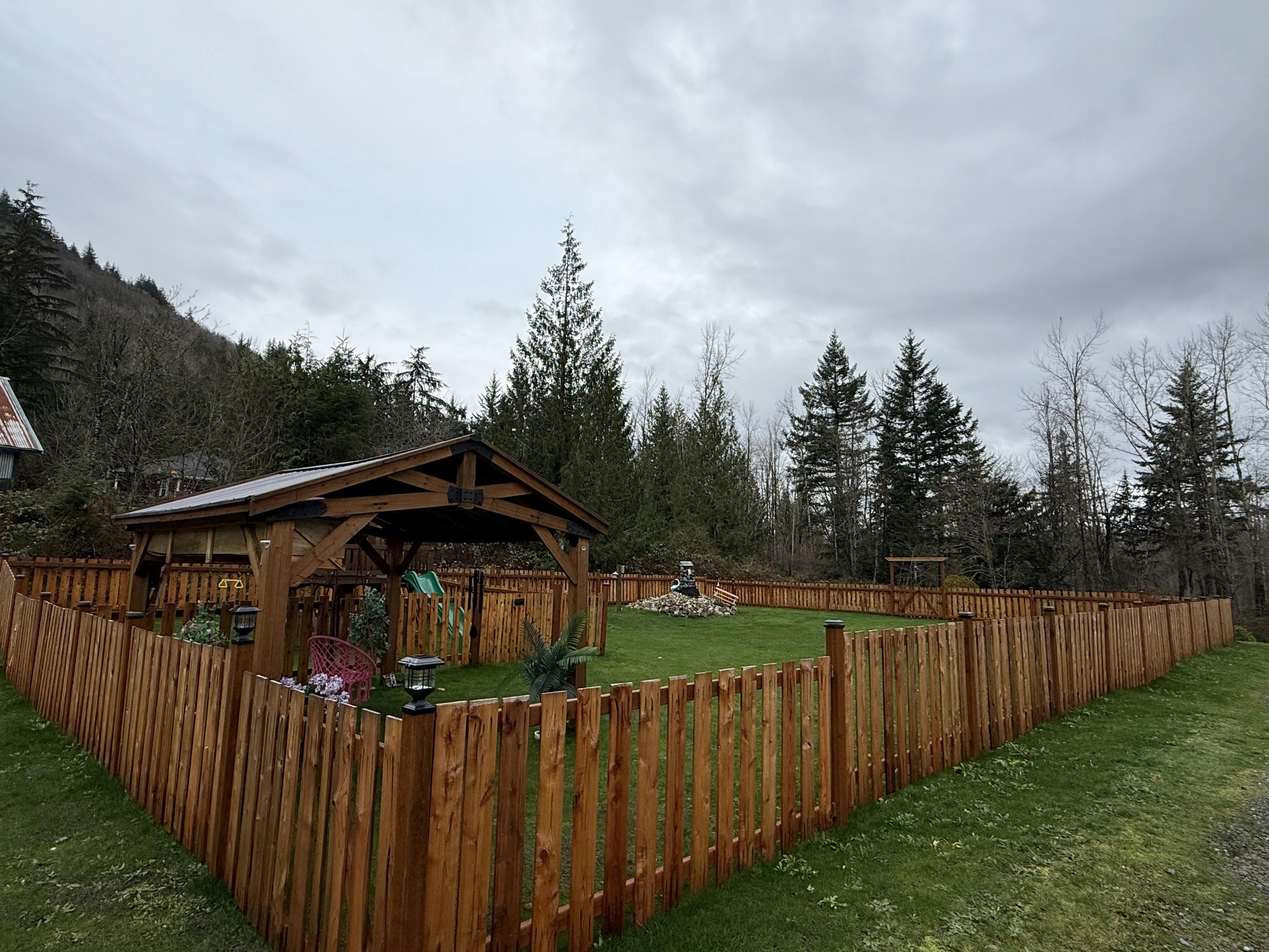 Wooden fence surrounding a grassy yard with a wooden gazebo and trees