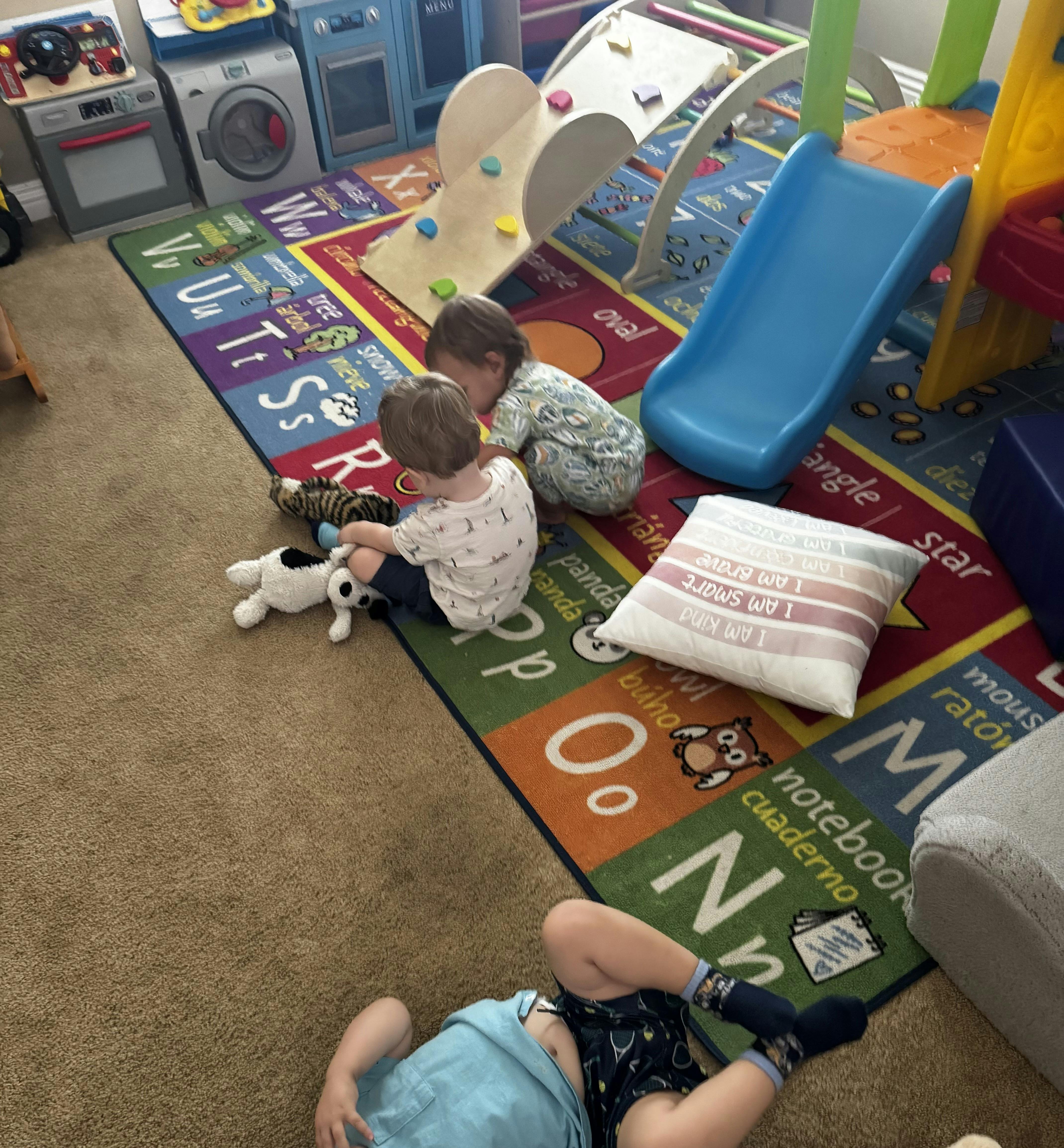 Three children playing with toys on an alphabet floor mat in a playroom