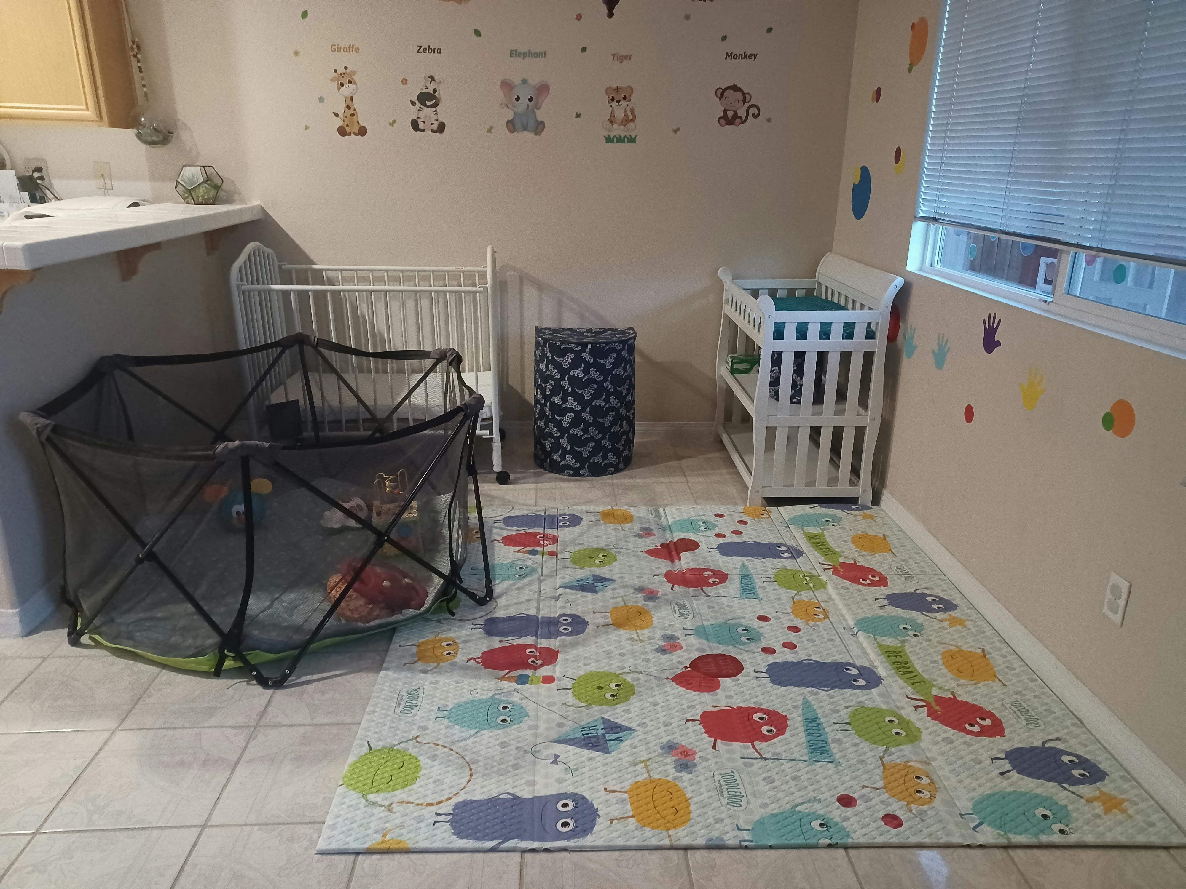 Playpen, crib, and changing table in a room with a colorful playmat