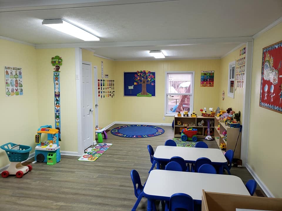 A brightly lit classroom with small tables and chairs, toys, and colorful decorations