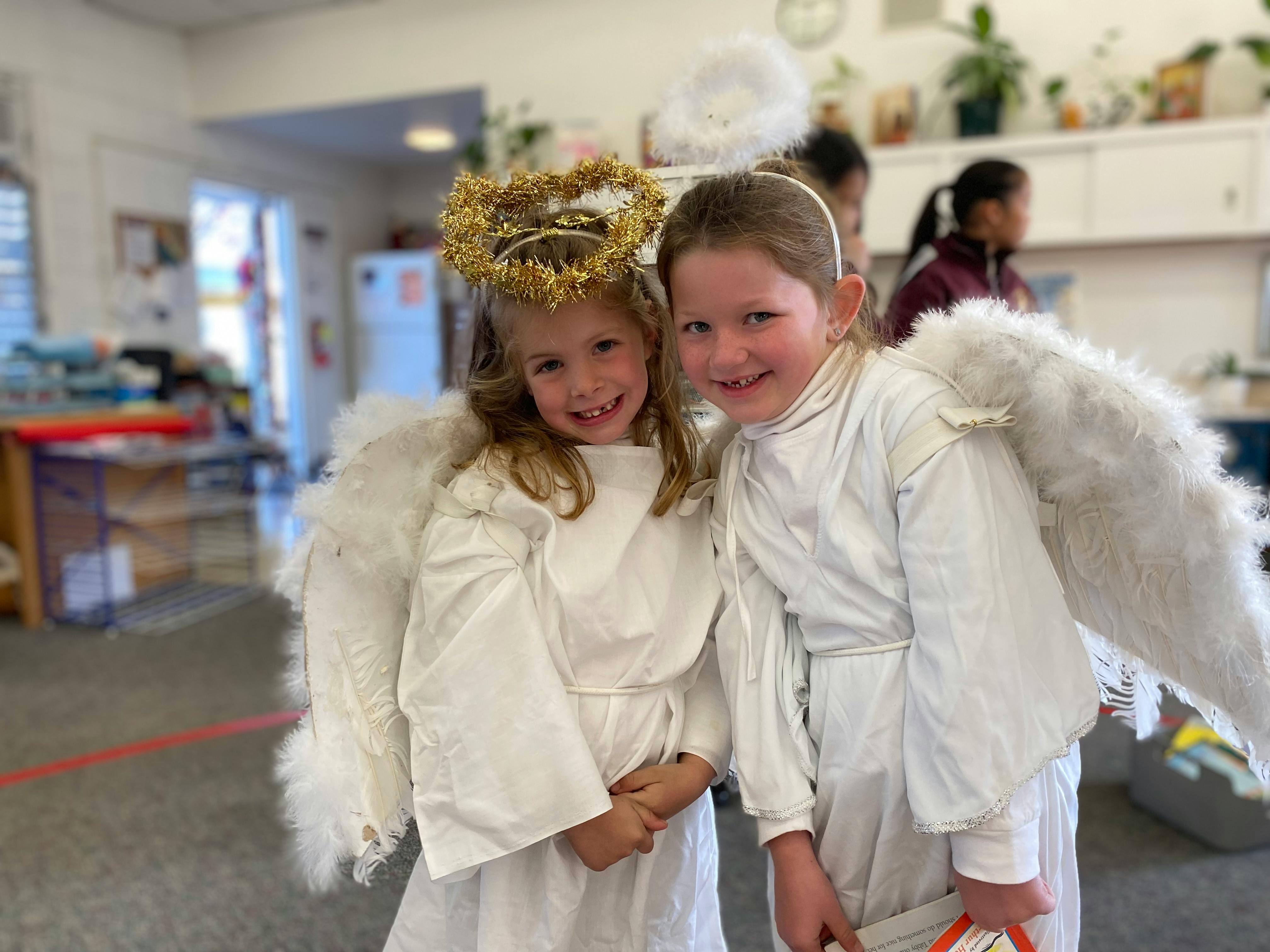Two children in white angel costumes with wings and halos