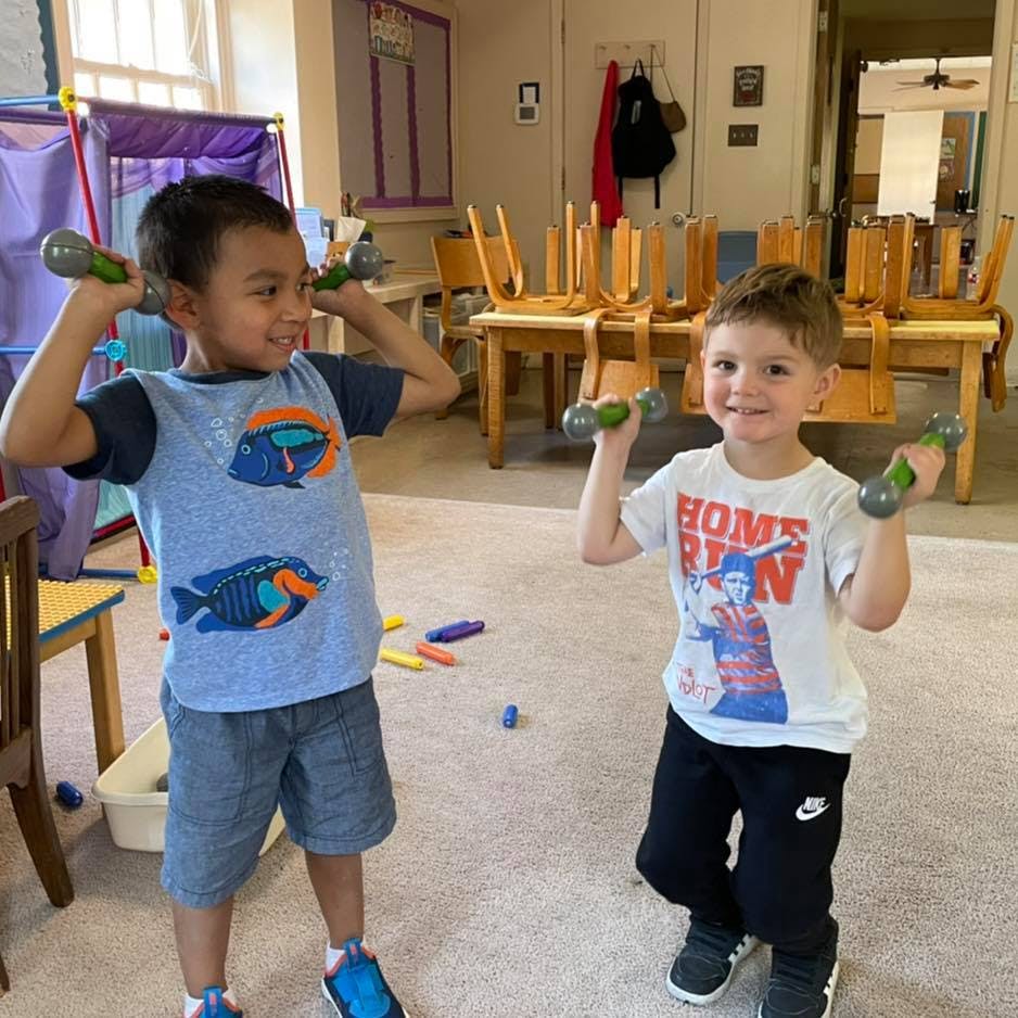 Two children holding small dumbbells in a classroom