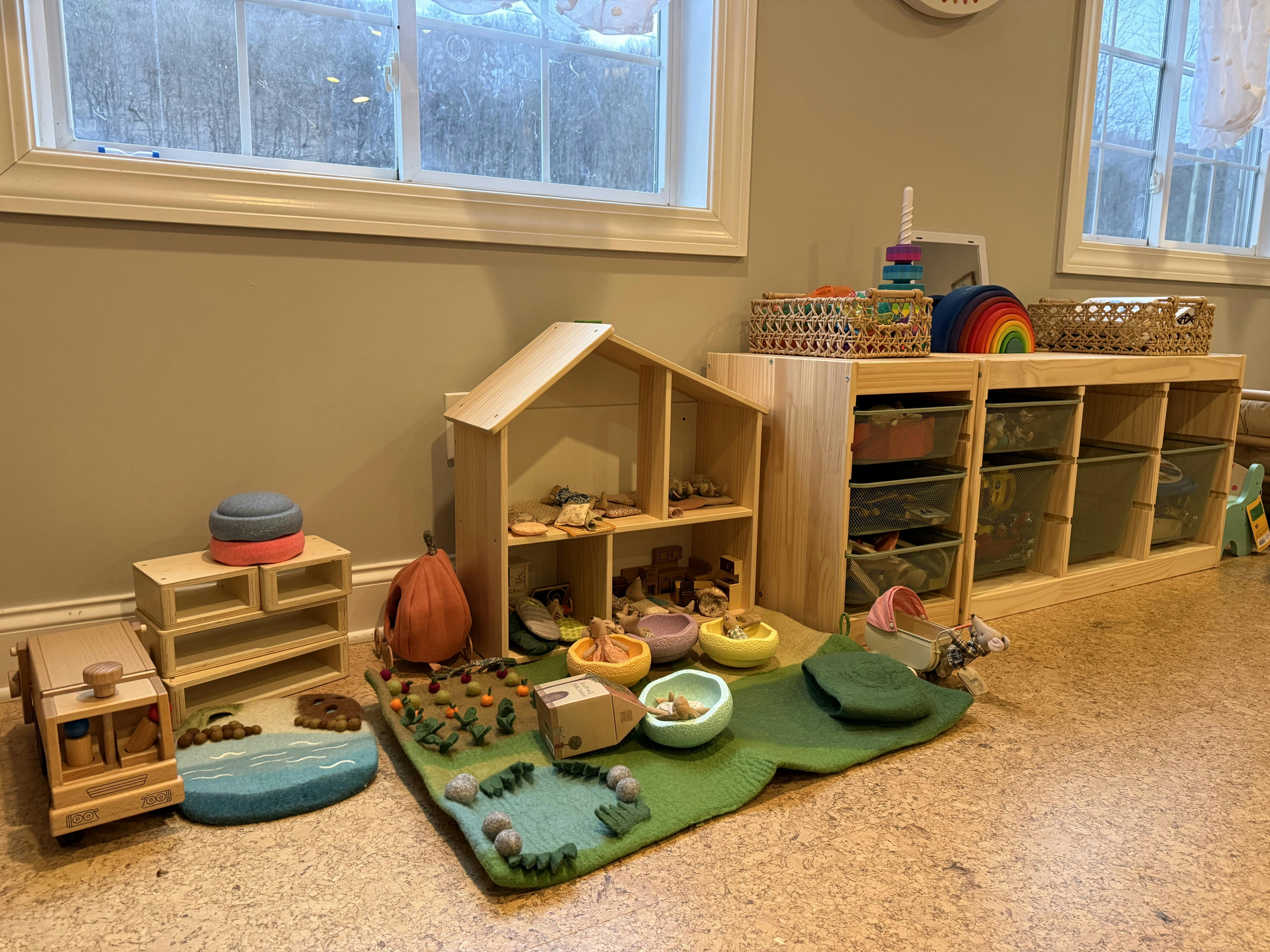 Children's play area with wooden dollhouse, toy stroller, and felt play mats