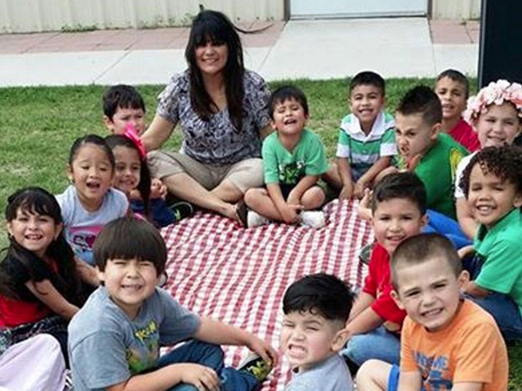 Adult and many children sitting on a red and white blanket outdoors