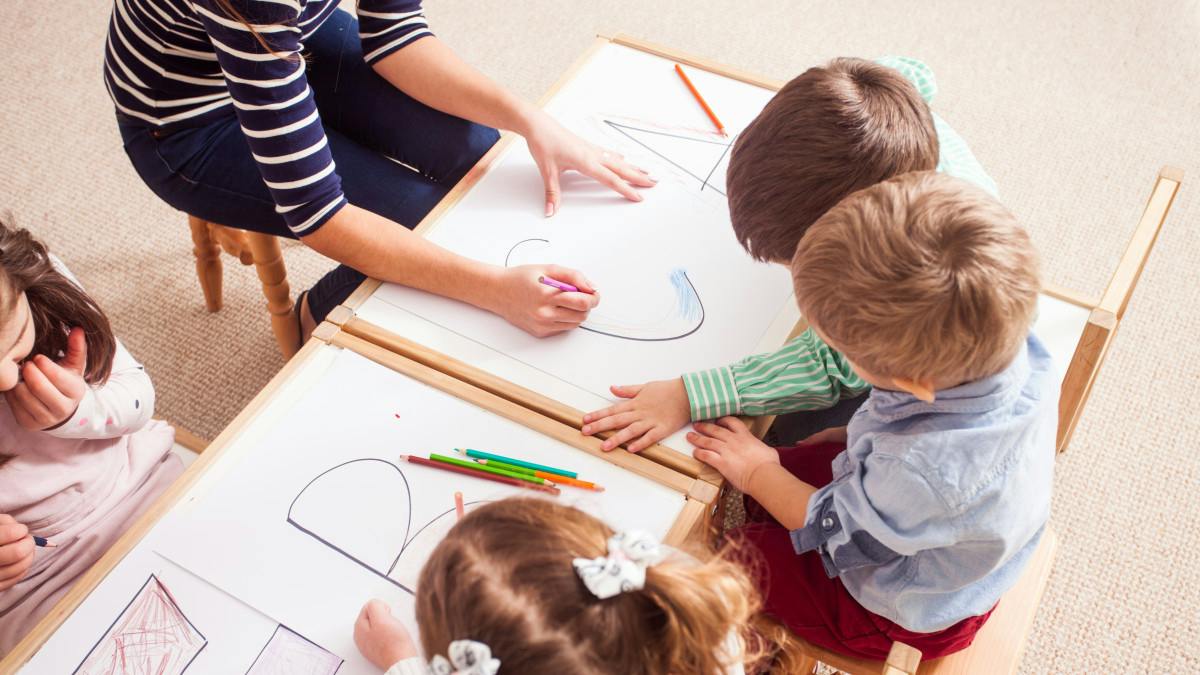 Adult and children drawing on papers at tables