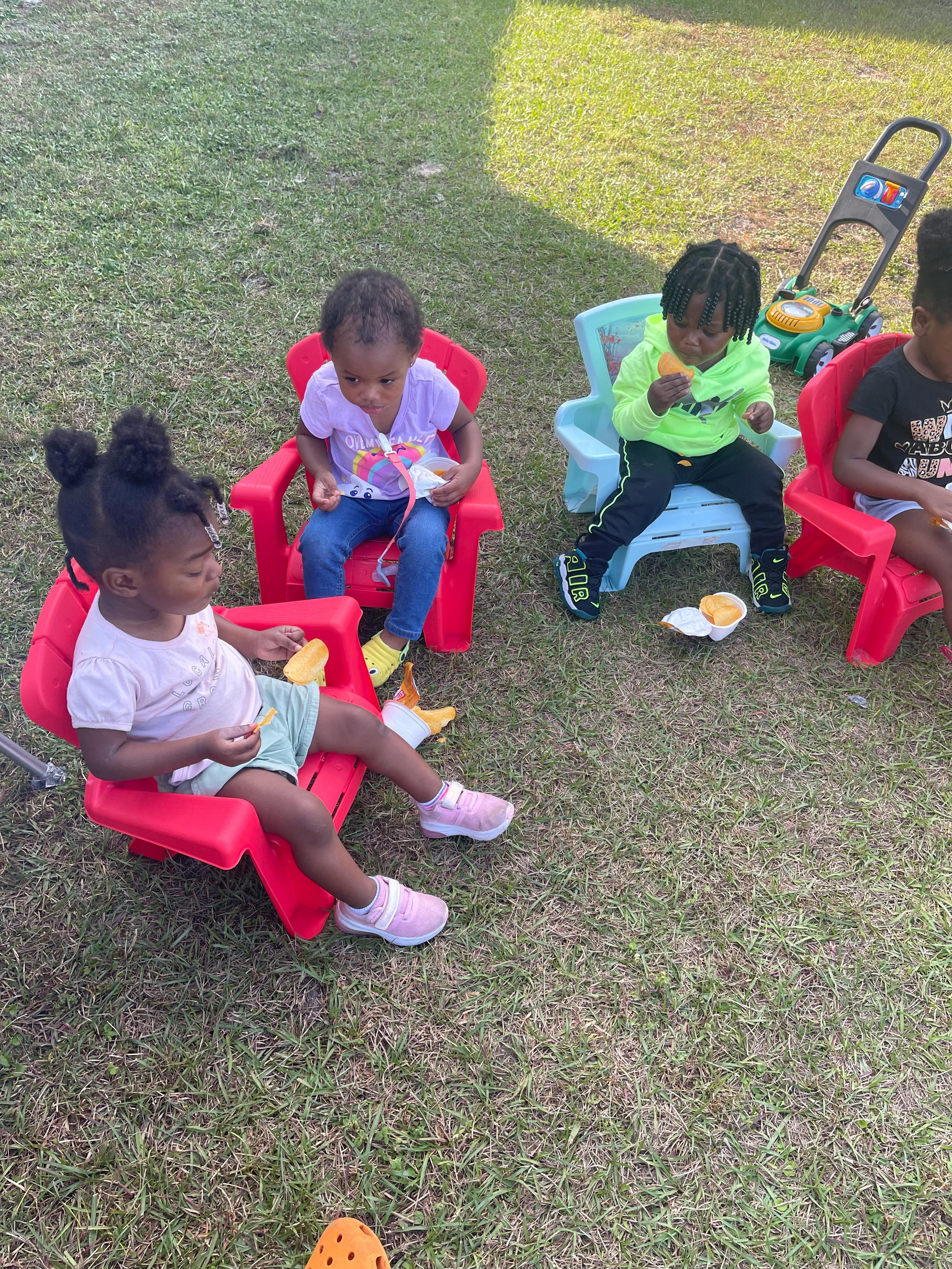 Three children sitting in chairs on grass