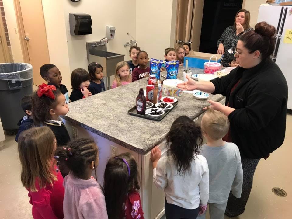 Adult speaking to a group of children gathered around a counter