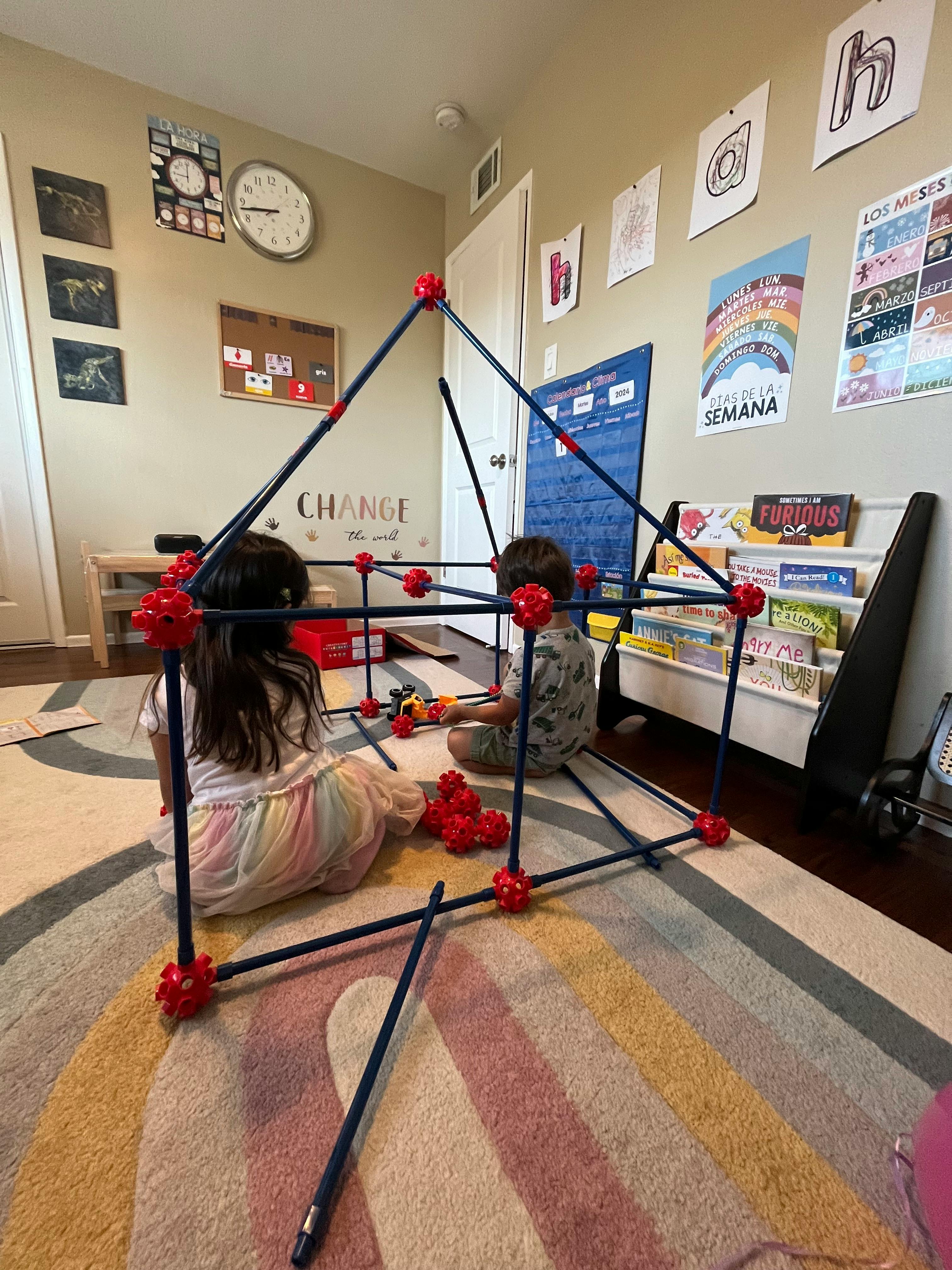 Two children building a fort with construction toys on a rainbow rug
