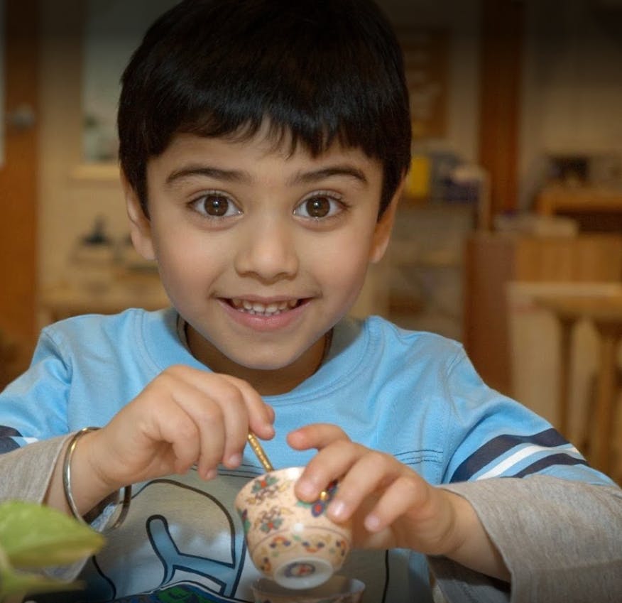 Child holding a small patterned cup with a spoon