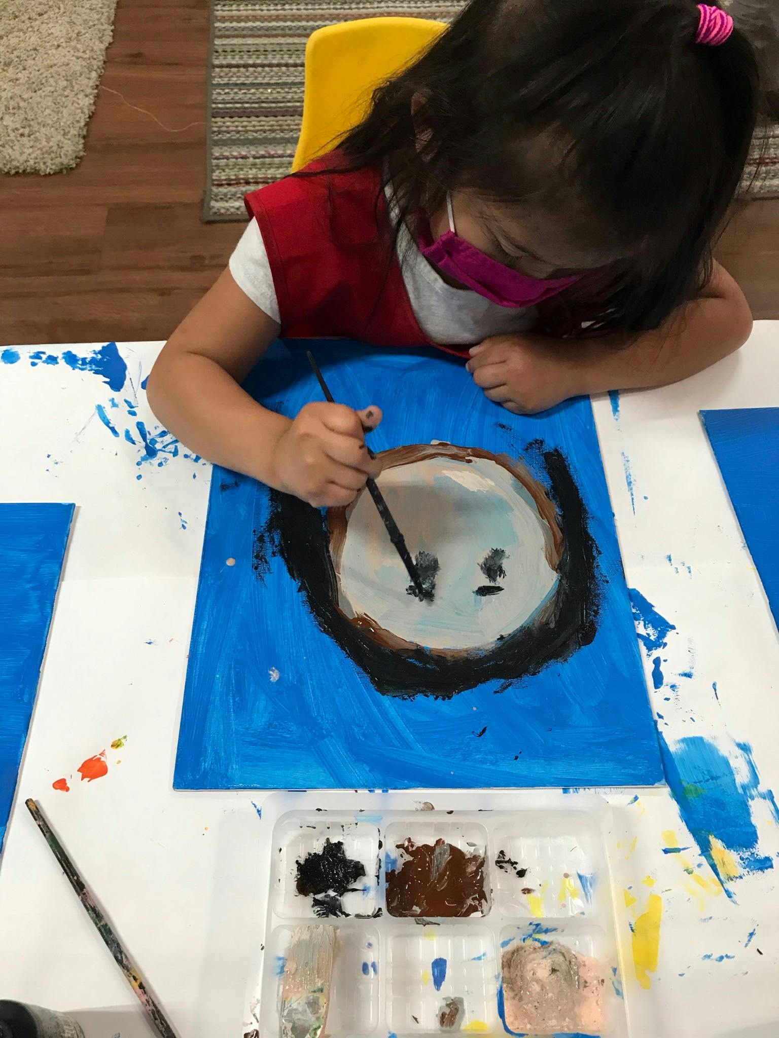 Child in a mask painting on blue paper