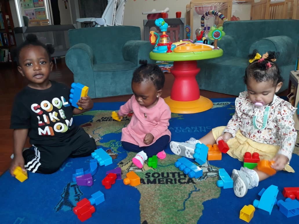 Three children playing with colorful building blocks on a map rug