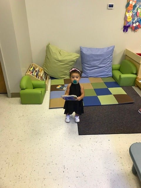 Child with pacifier holding a book in a classroom