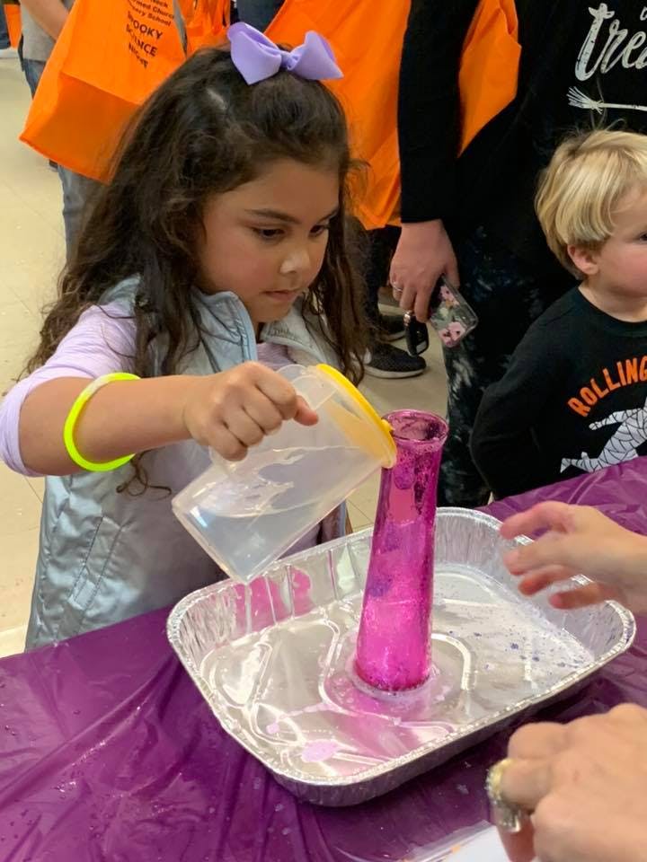 Child pouring liquid from a pitcher into a pink vase