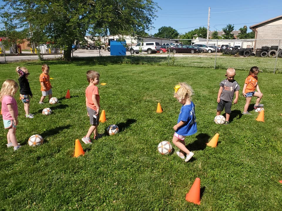 Children playing soccer with cones on a grassy field