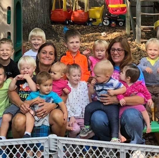 Two people with a group of children and babies outdoors