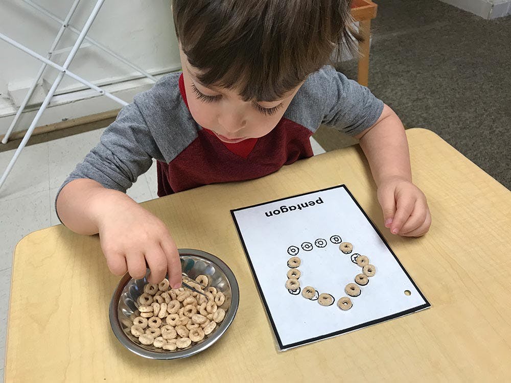 Child placing cereal pieces on a paper with a shape outline of a shape