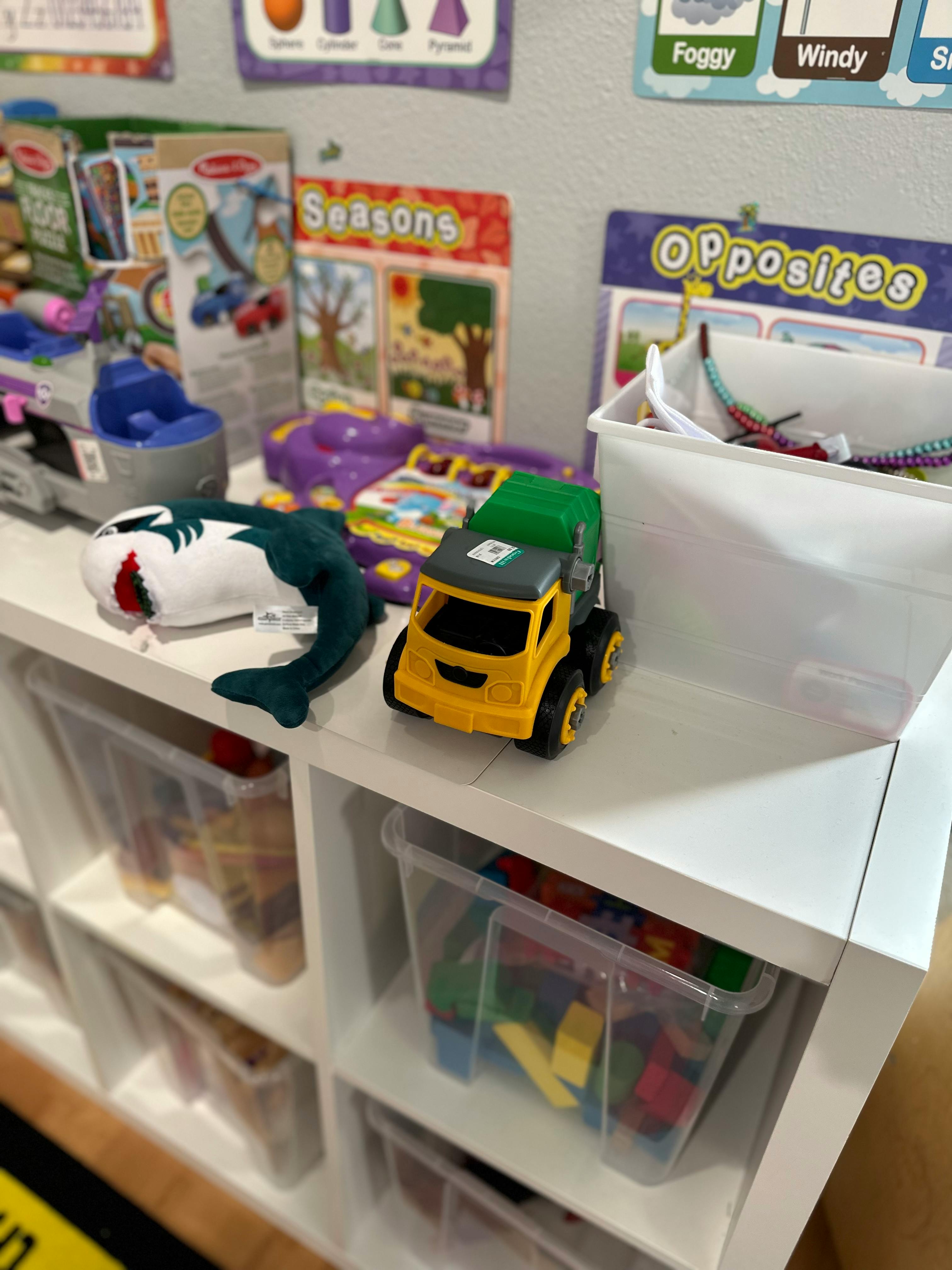 Toy shark and truck on a shelf with clear bins of toys