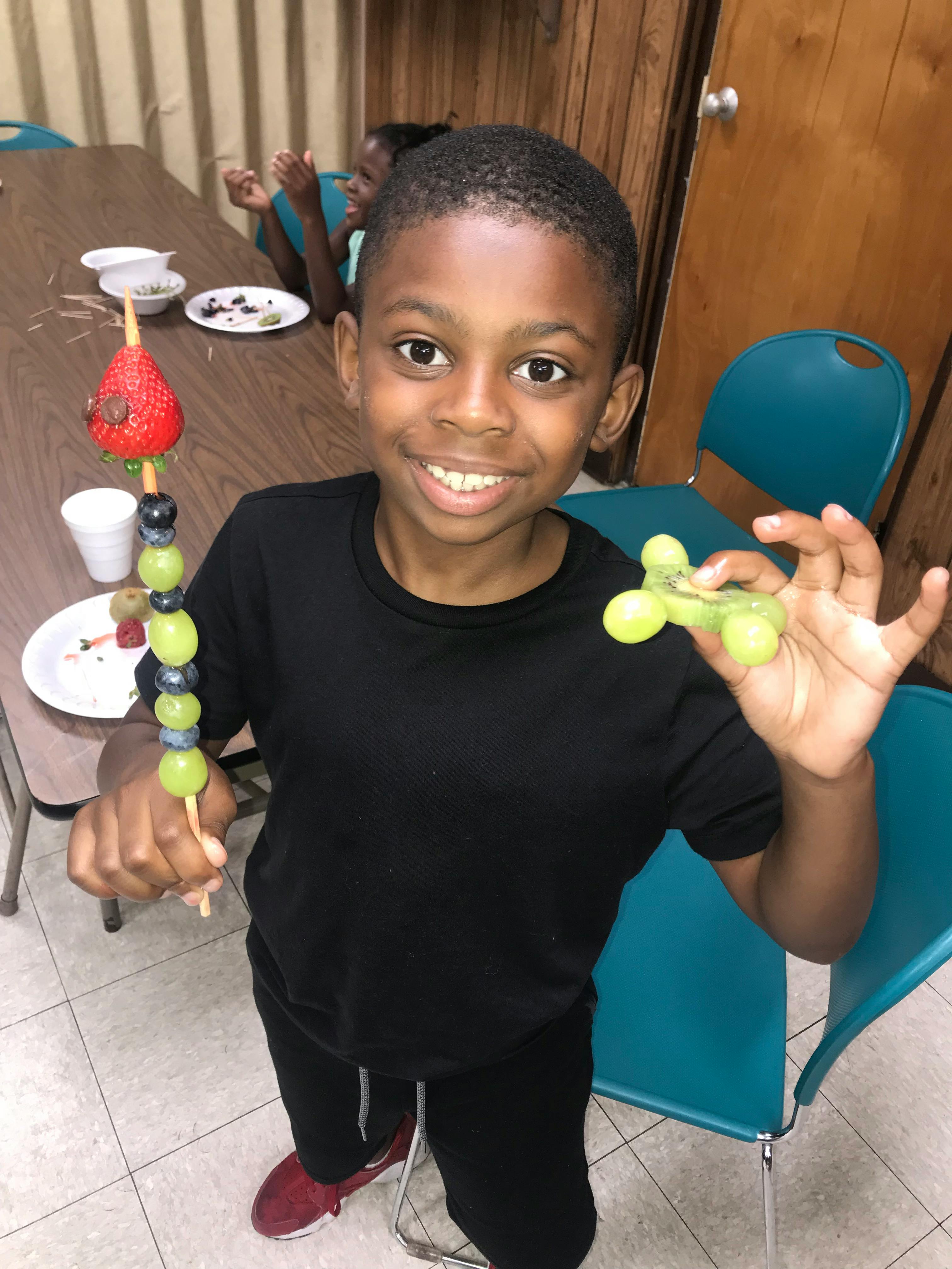 Child holding a fruit skewer and a small green object