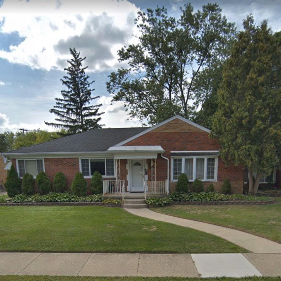 Brick house with a white front door and porch, green lawn, and trees