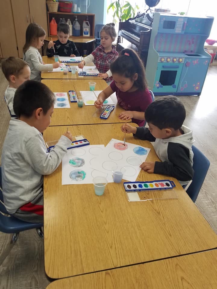 Children painting at tables in a classroom