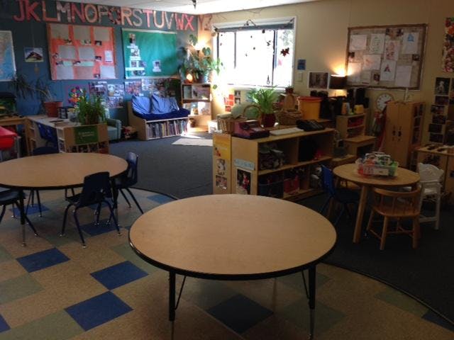 Classroom with round tables and chairs, shelves, and a window