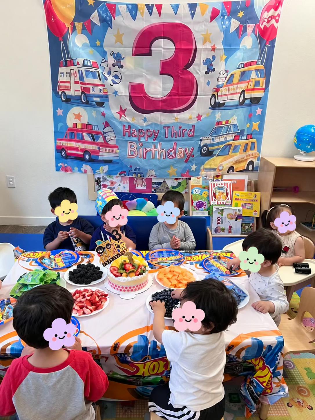 Children sitting at a table with fruit and a cake for a third birthday party