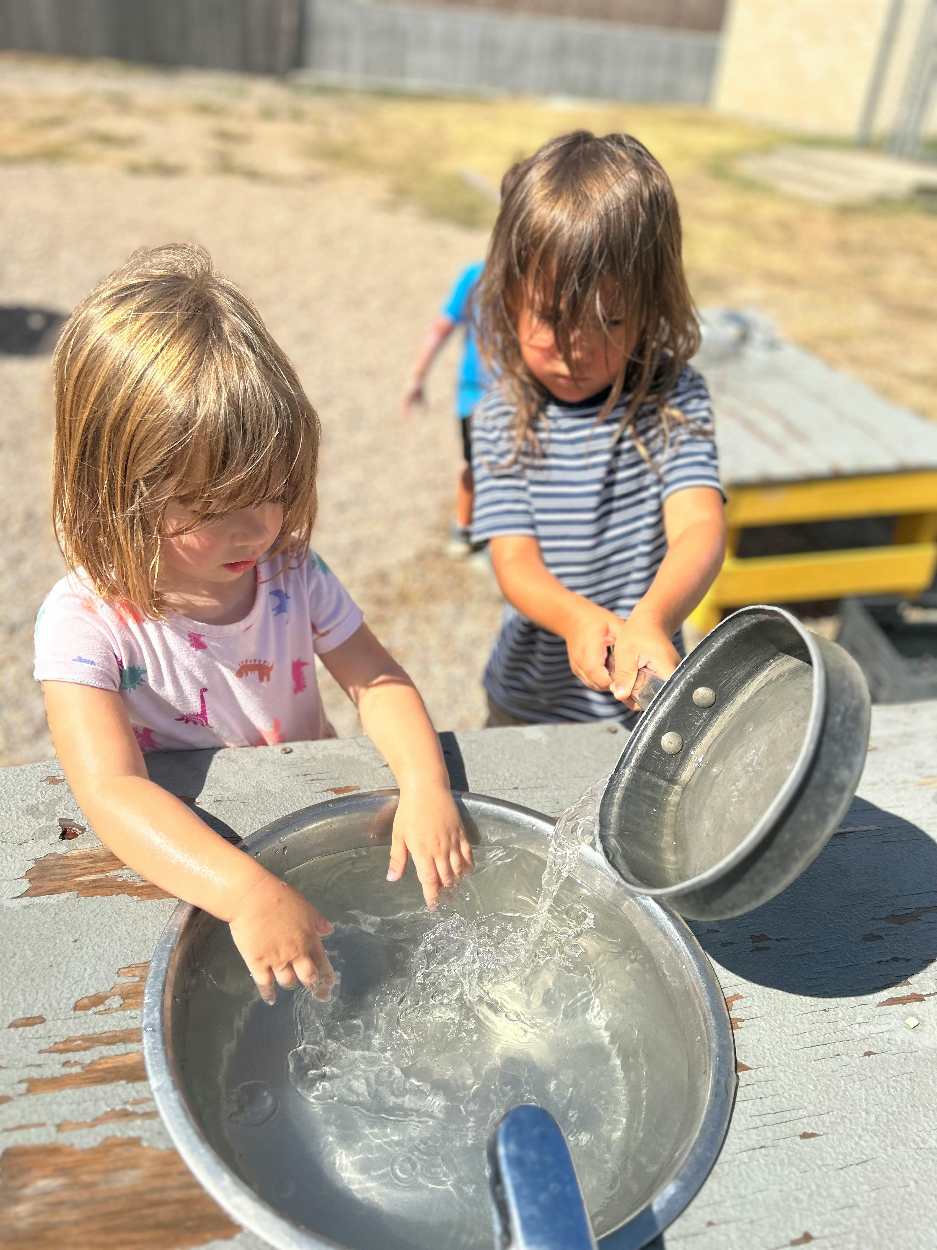 Two children playing with water in metal bowls