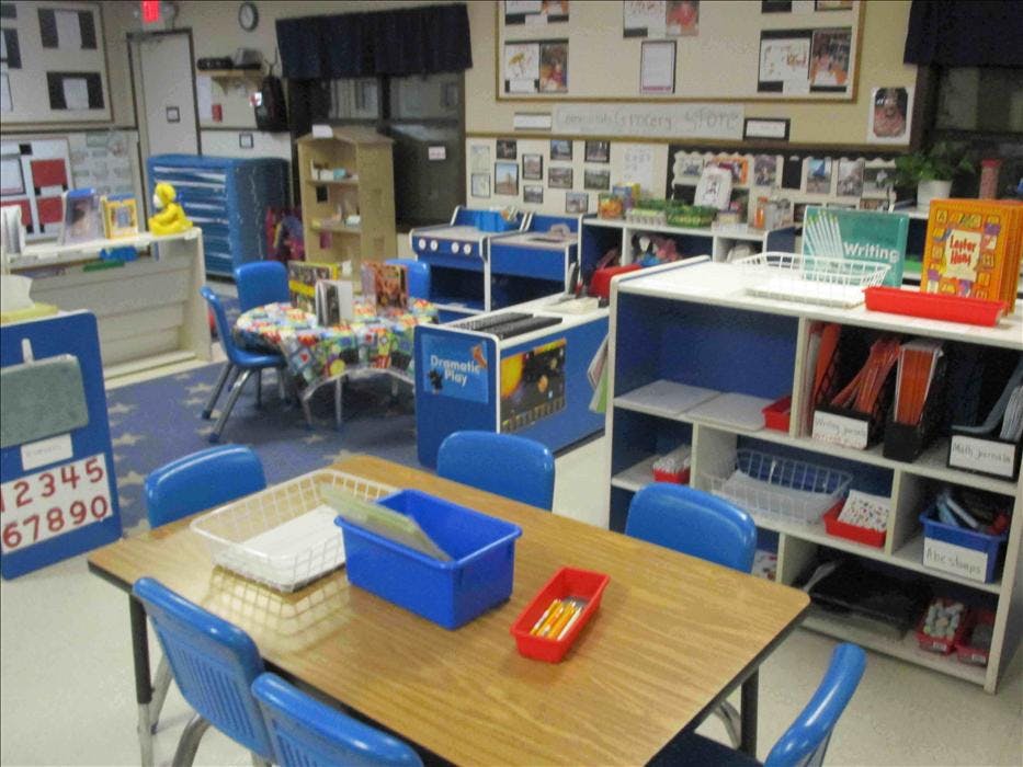 Classroom with small tables and chairs, shelves, and a \"Dramatic Play\" area
