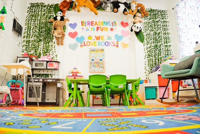 Children's play area with small table and chairs, toy kitchen, and colorful rug