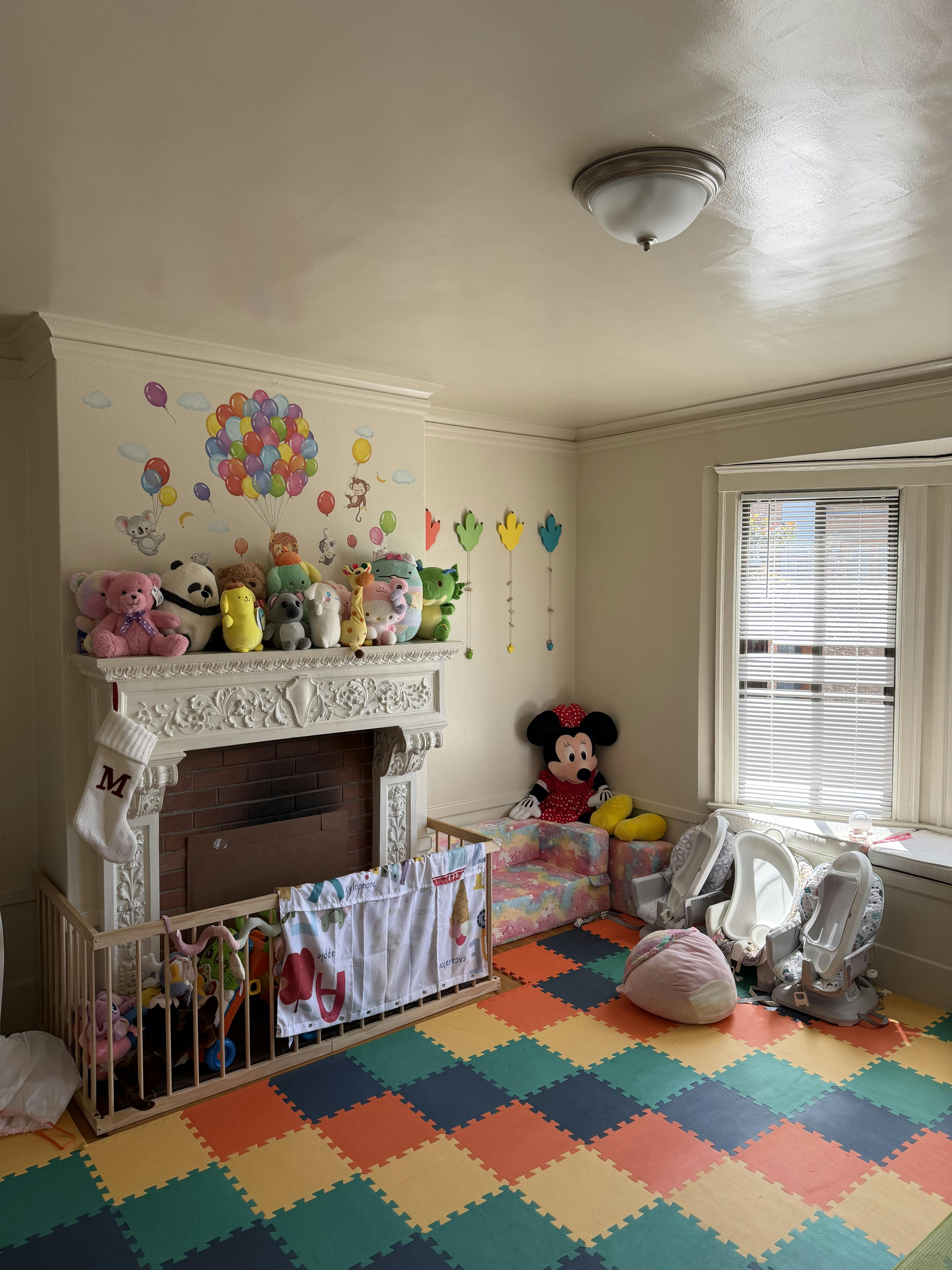 Playroom with colorful floor mats, a fireplace adorned with stuffed animals, and baby equipment