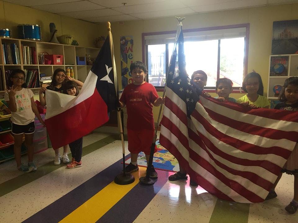 Children holding Texas and American flags indoors