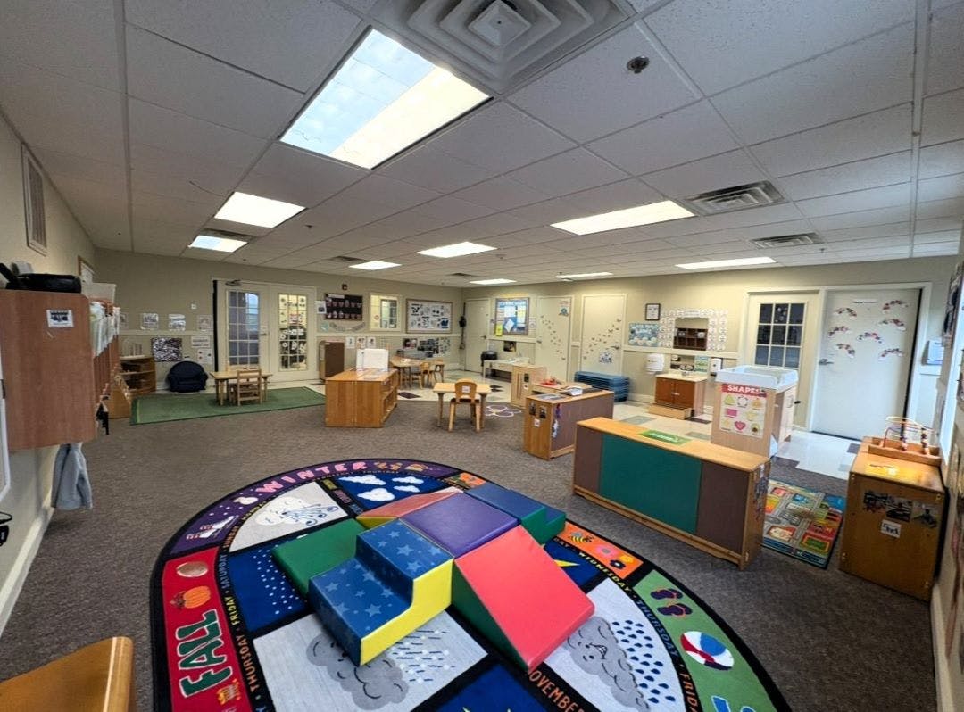 Classroom with small tables, chairs, and play equipment including a colorful rug