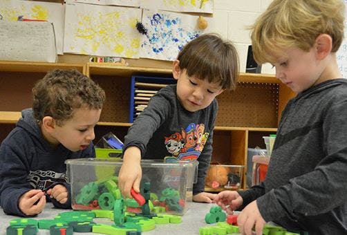 Three children playing with building blocks in a classroom