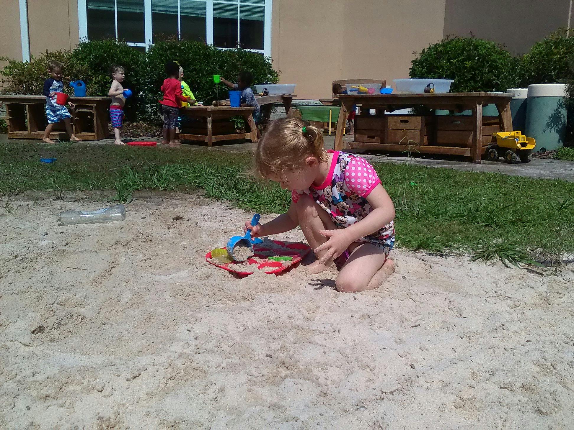 Child kneeling in sand playing with toys