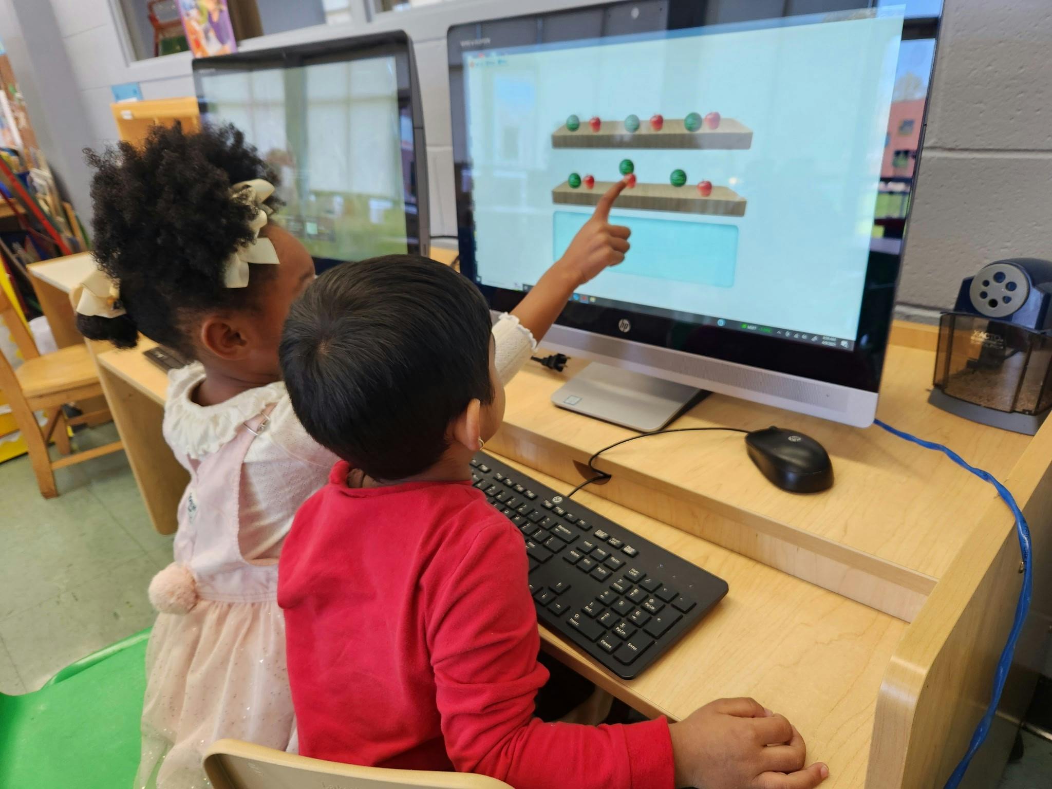 Two children looking at a computer screen, one pointing at the screen