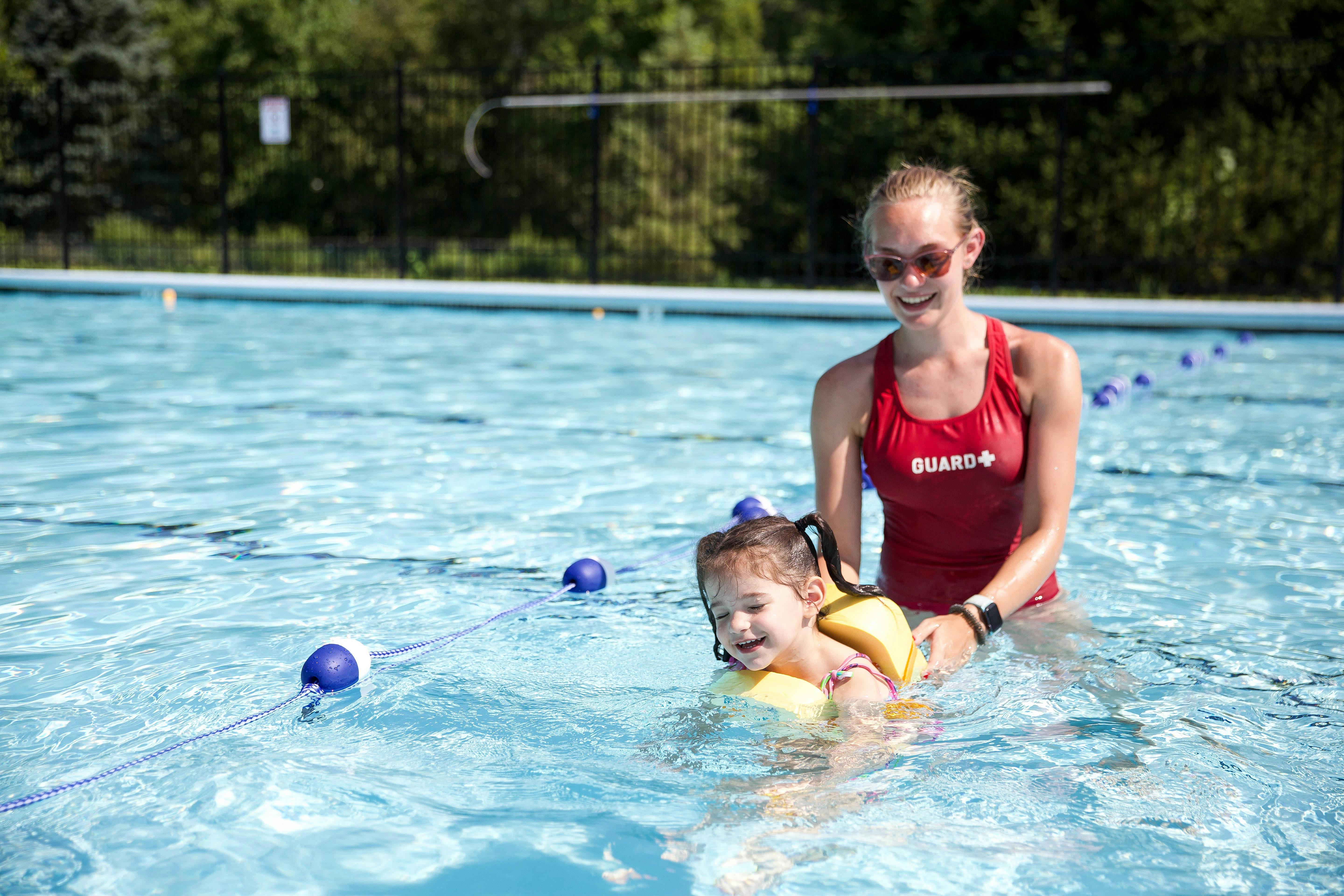Person in red swimsuit helping child in yellow floaties in a swimming pool