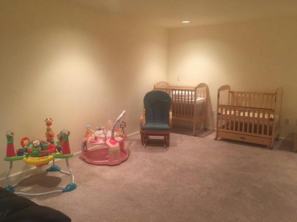 Two cribs, a rocking chair, and baby play equipment in a room