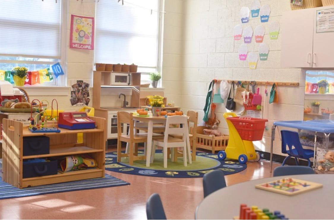 Classroom with small tables and chairs, play kitchen, and toy shopping cart