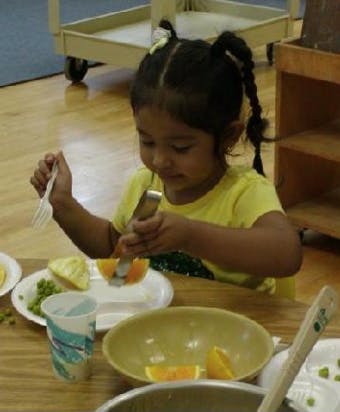 Child using a knife and fork to cut an orange