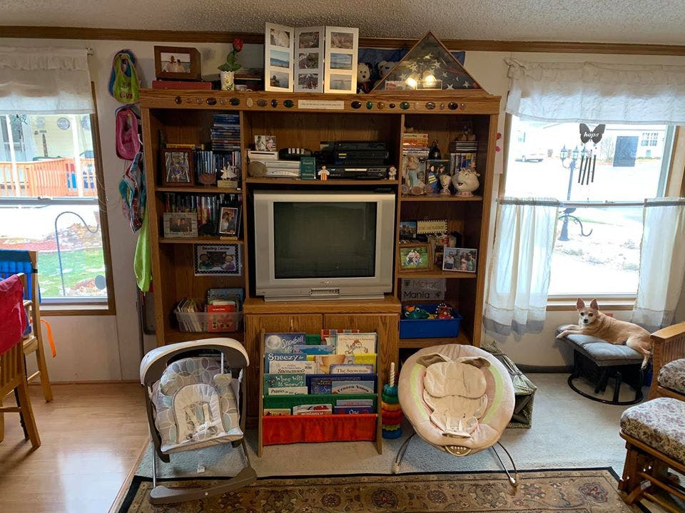 Living room with a wooden entertainment center, television, and baby items