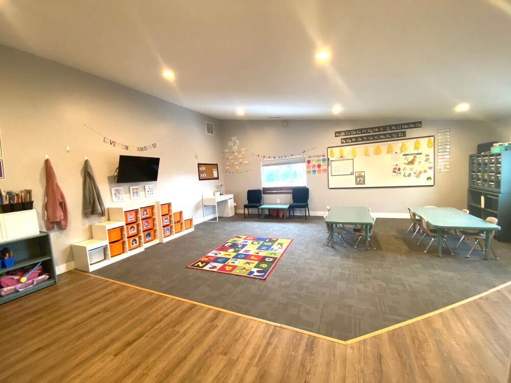 Classroom with small tables and chairs, a colorful rug, and a whiteboard